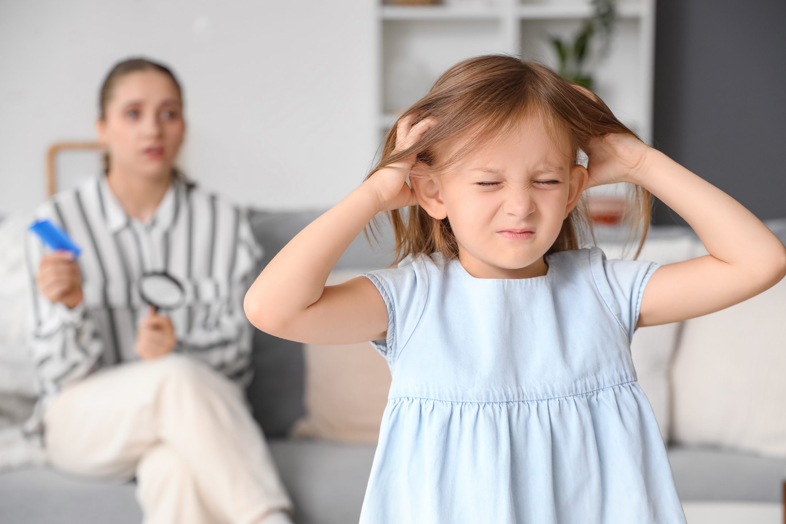 Child scratching her scalp while a parent prepares to check for lice