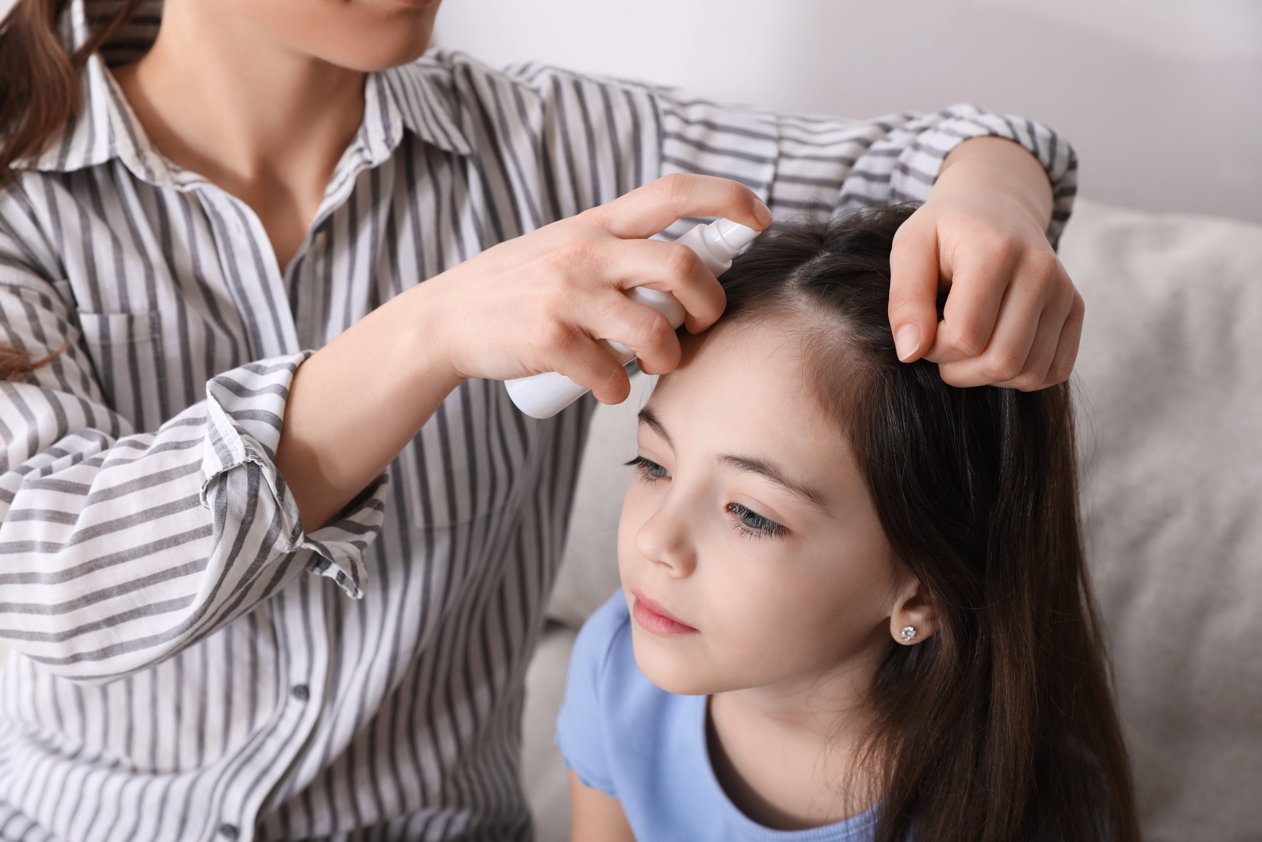 Parent applying lice treatment spray while checking a child?s hair