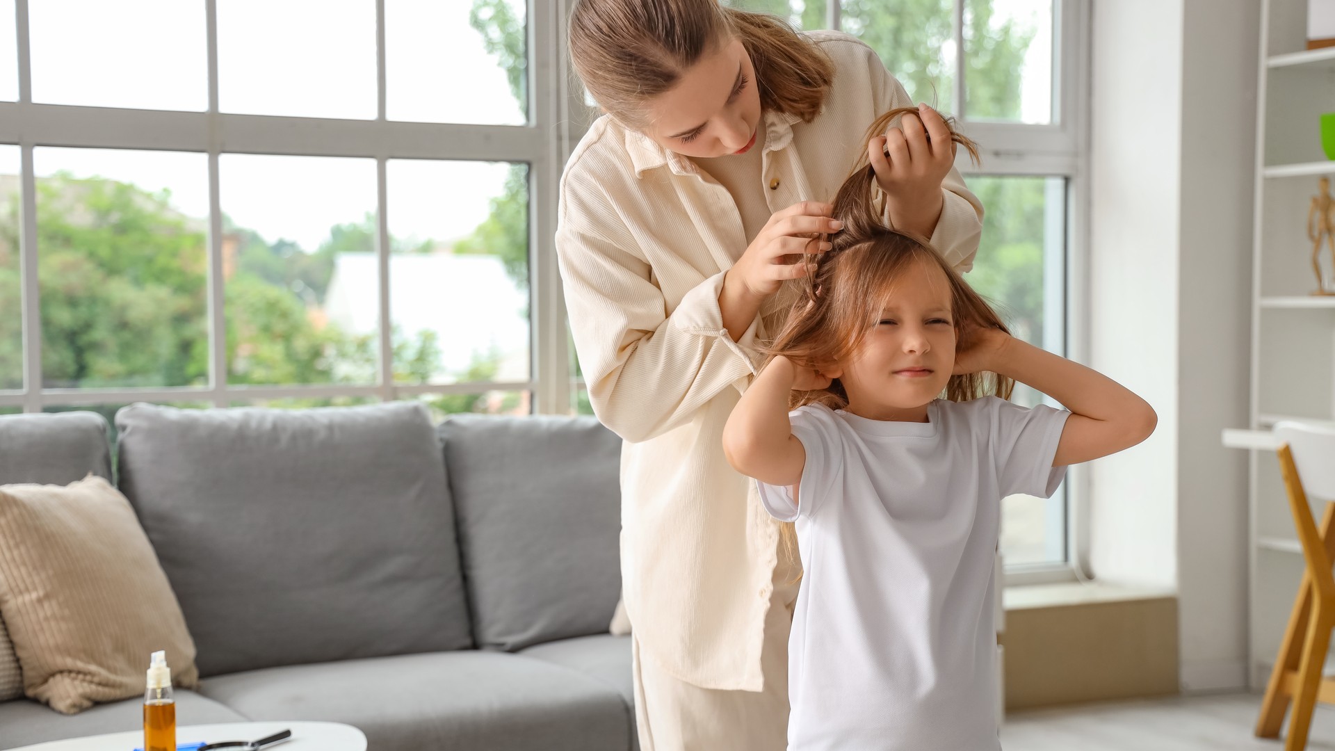 A Union County mother carefully parting and checking her daughter's hair for head lice at home, the exact visual decision moment a parent faces during the first week after a known exposure.