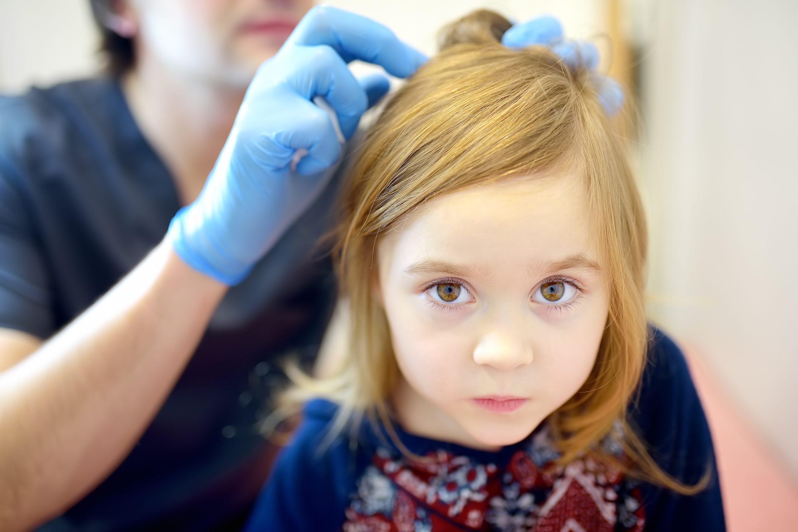 A clinician parts a young girl's hair under bright light to examine her scalp and identify whether lice are present