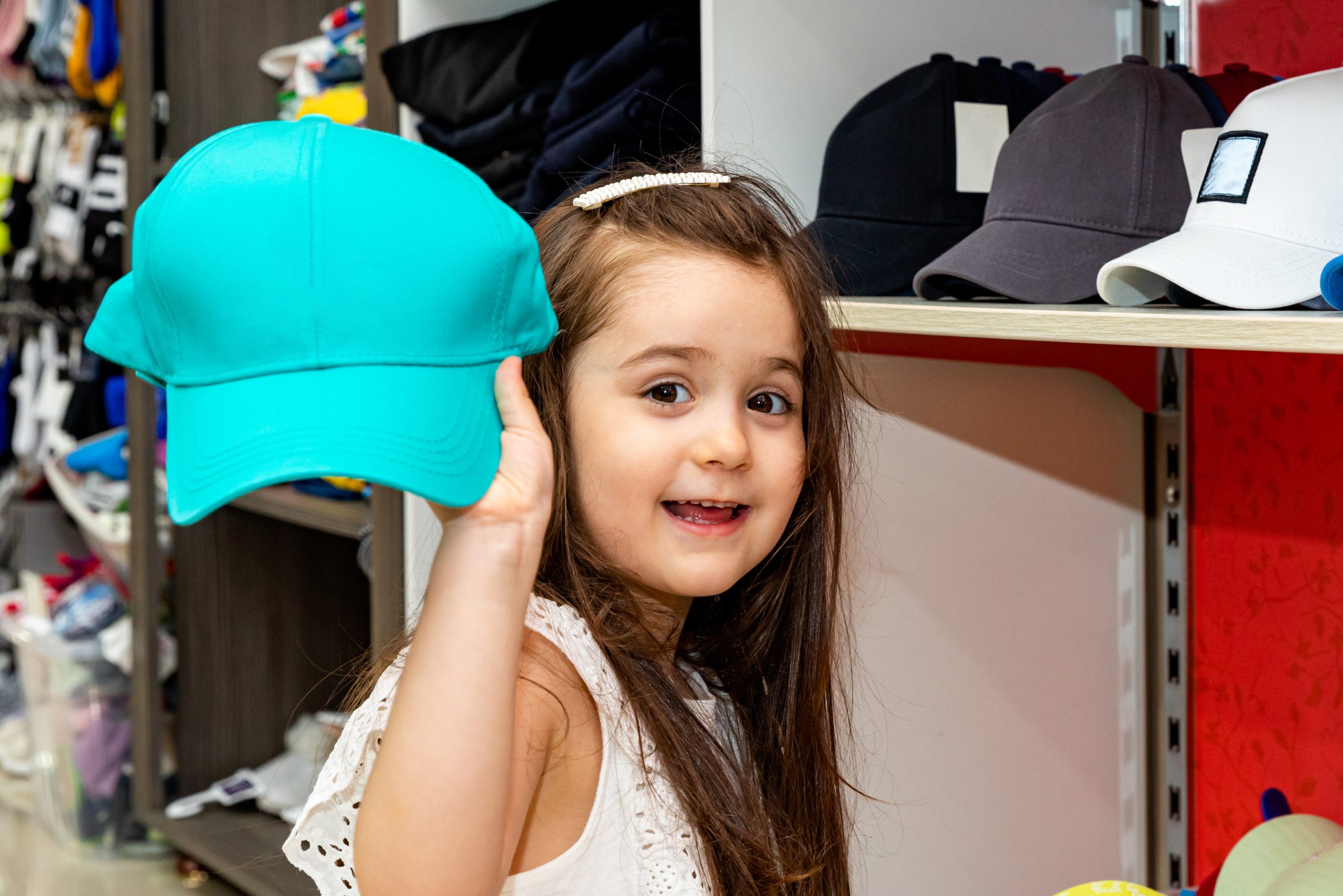 A young girl trying on a baseball cap in a clothing store, the kind of quick hat try-on parents worry might pass along head lice