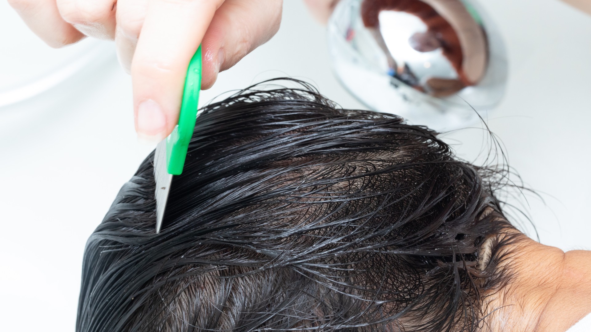 Professional using a fine-tooth lice comb on a child's wet hair, the real removal method a shower cannot replace