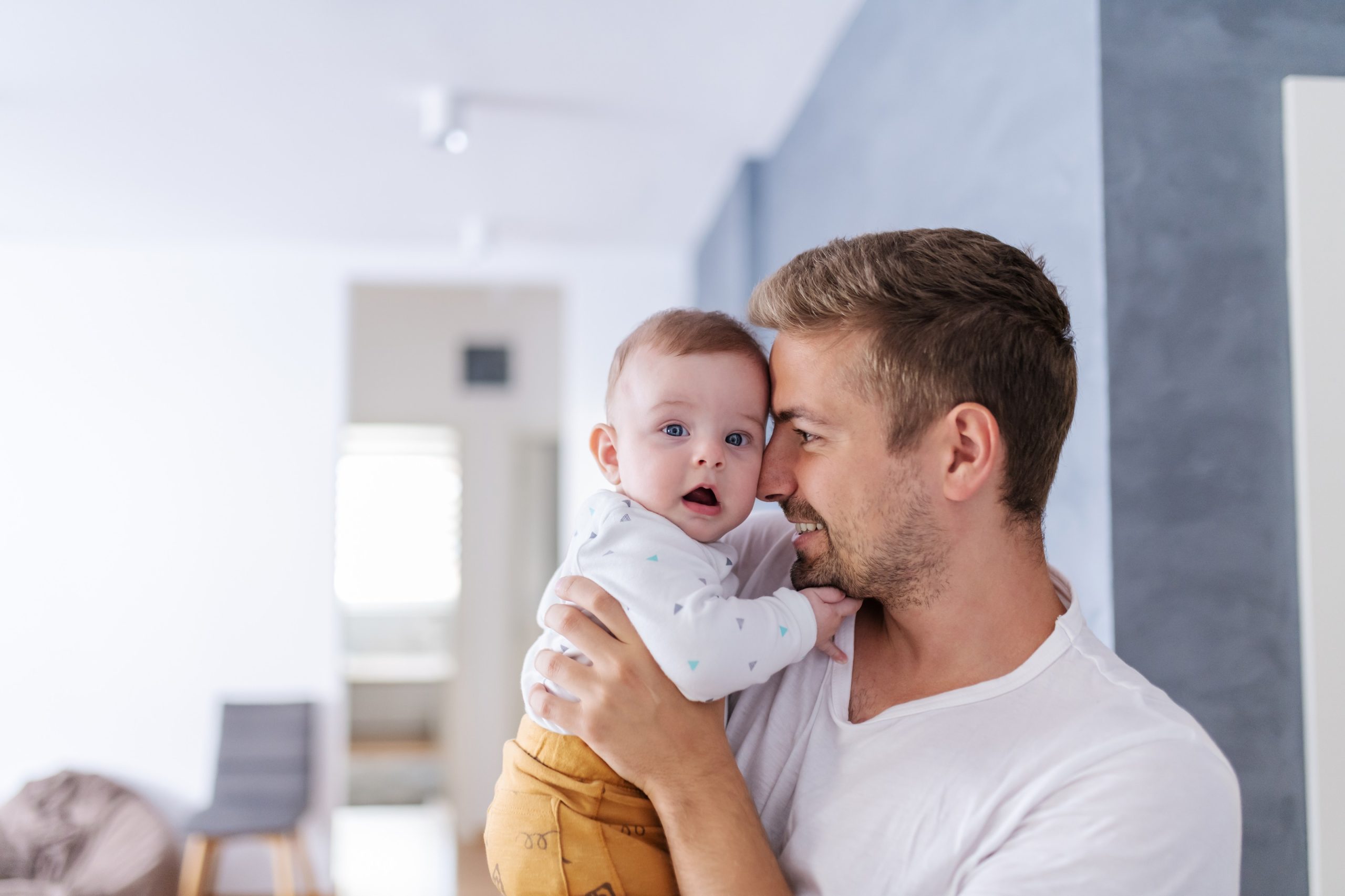 Adult with short facial hair holding a baby close to their cheek