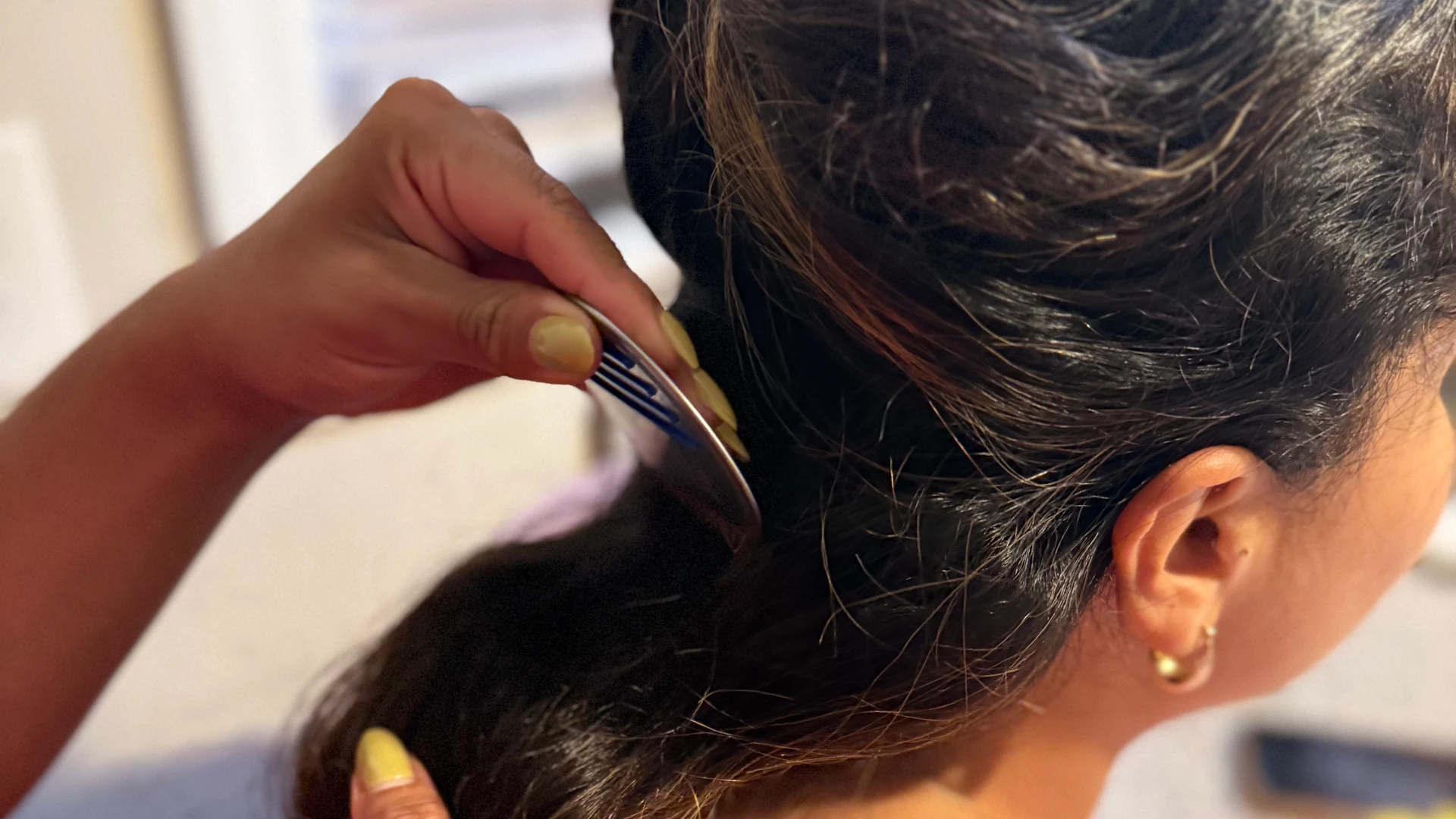 Hand drawing a comb through dark hair near an ear