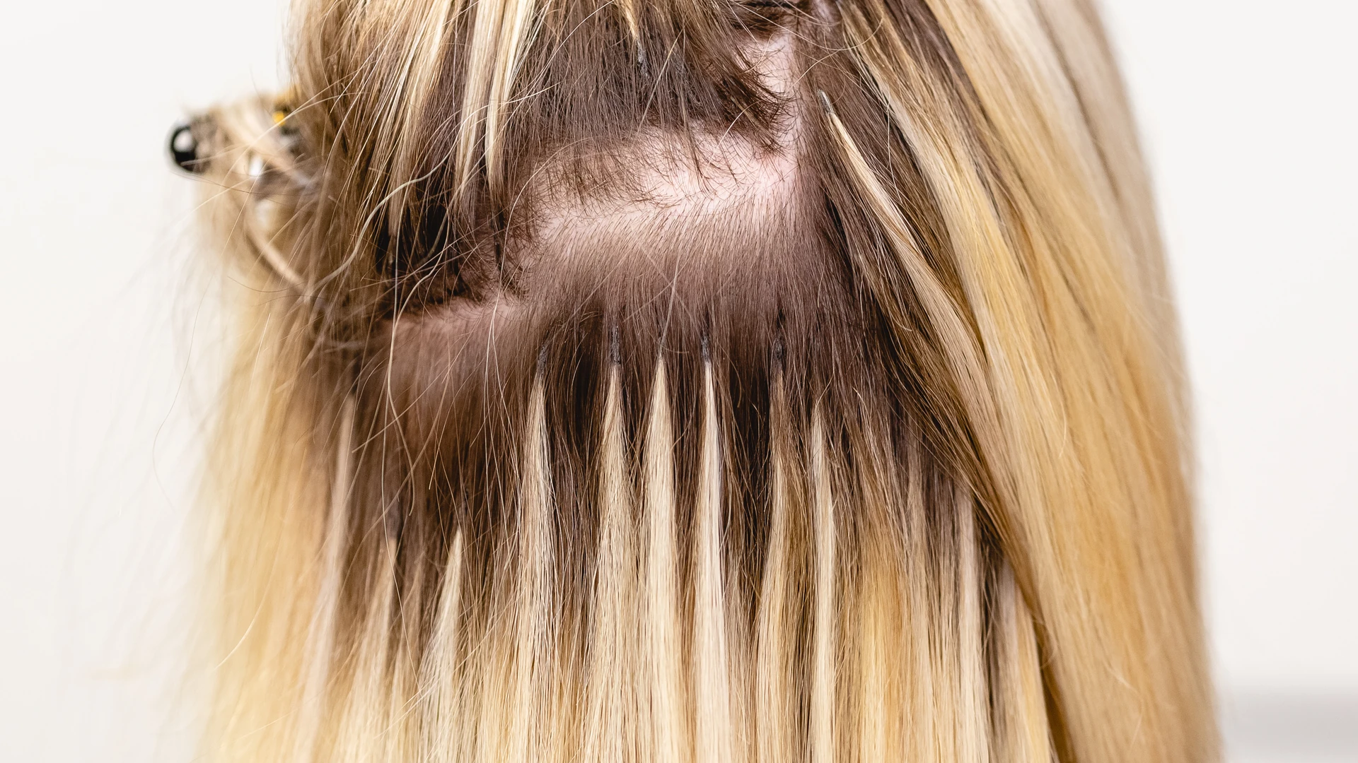 Row of hair extensions visible beneath a lifted section of blonde hair
